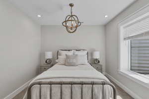Recessed ceiling lighting, a prominent spherical chandelier, and a large window with white blinds illuminate this neutral-toned room