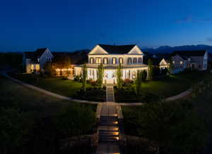 Colonial-style residence featuring a prominent covered porch with white columns, a multi-tiered stone-clad staircase, and expansive manicured lawns