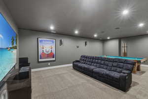 Dedicated media room featuring a large projection screen, recessed lighting, wall-mounted speakers, and a pool table