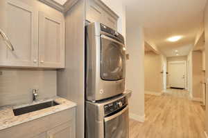 Dedicated laundry area featuring stacked appliances, a utility sink with a stone-finish countertop, and light-toned cabinetry