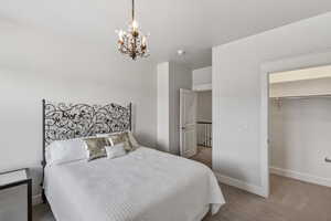 Bedroom with a decorative wrought iron headboard, an ornate chandelier, neutral carpeting, white trim, and a visible closet with shelving