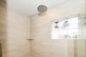 Shower stall featuring neutral-toned horizontal tile, a ceiling-mounted rainfall showerhead, a built-in corner shelf, and a frosted window with grid detailing