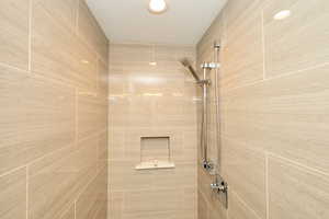 Tiled shower enclosure featuring light-toned large format tiles, a recessed niche, a handheld shower fixture, and polished chrome hardware