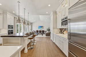 Expansive kitchen featuring wood-finish flooring, white cabinetry, stainless steel appliances, and a large island with seating