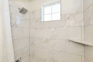 Shower enclosure featuring white marbled tile, a fixed rainfall showerhead, a built-in corner shelf, and a frosted window with grid
