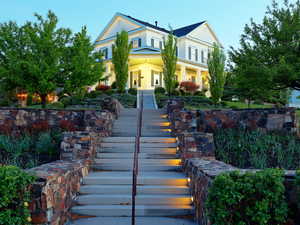 Grand exterior featuring a multilevel stone retaining wall, illuminated stone steps, and a landscaped terraced yard