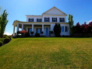 White two-story residence featuring a full-width covered porch with white columns, a light blue front door, dark blue window shutters, and a prominent front gable