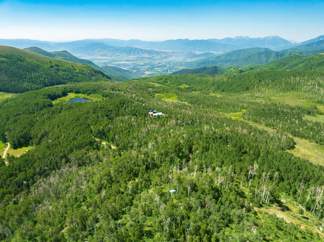 Expansive mountainous terrain featuring dense forests, a natural pond, and distant valley scenery