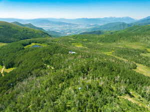 Expansive mountainous terrain featuring dense forests, a natural pond, and distant valley scenery