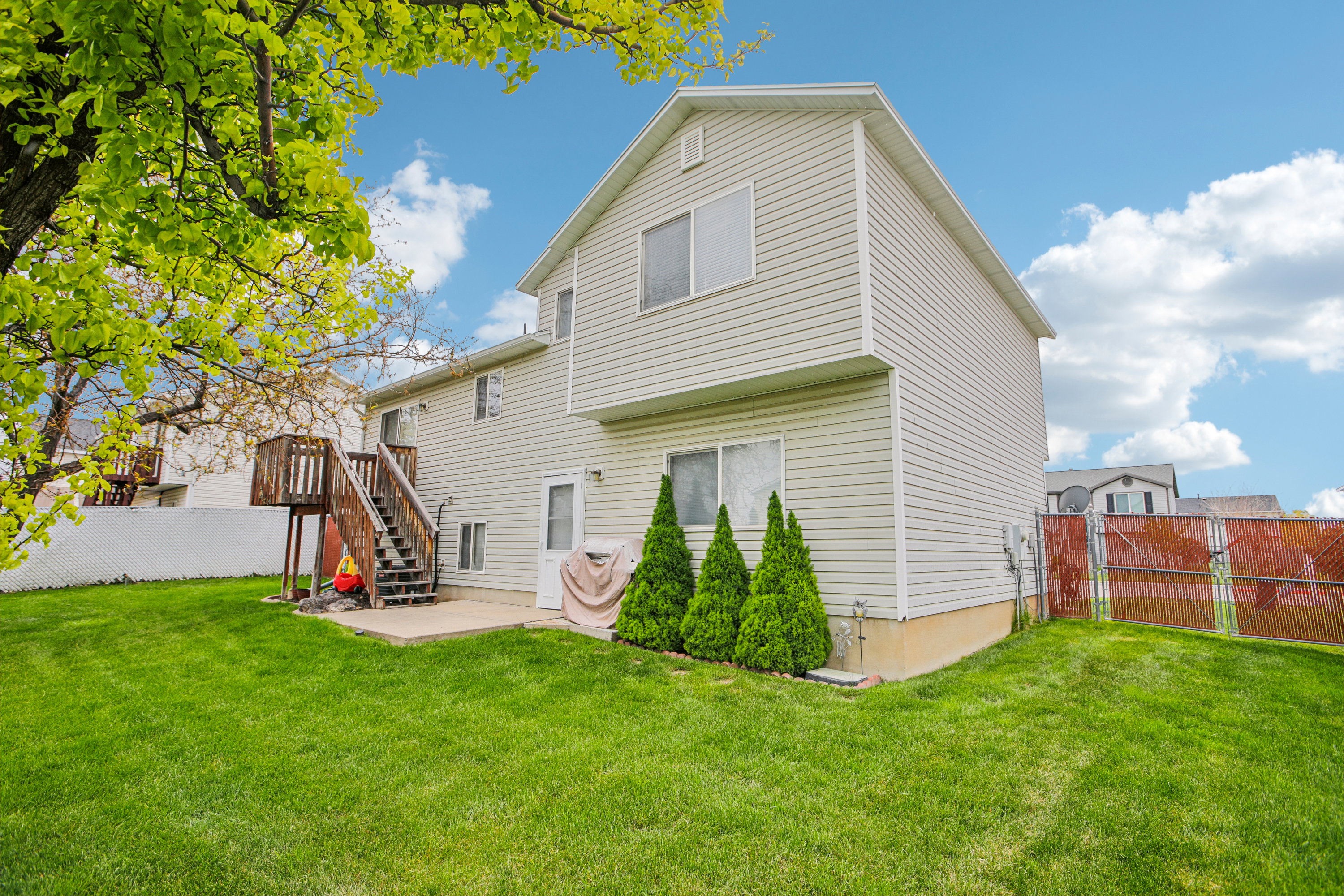 Expansive grassy backyard featuring a concrete patio, a multi-level wood deck, and mature landscaping