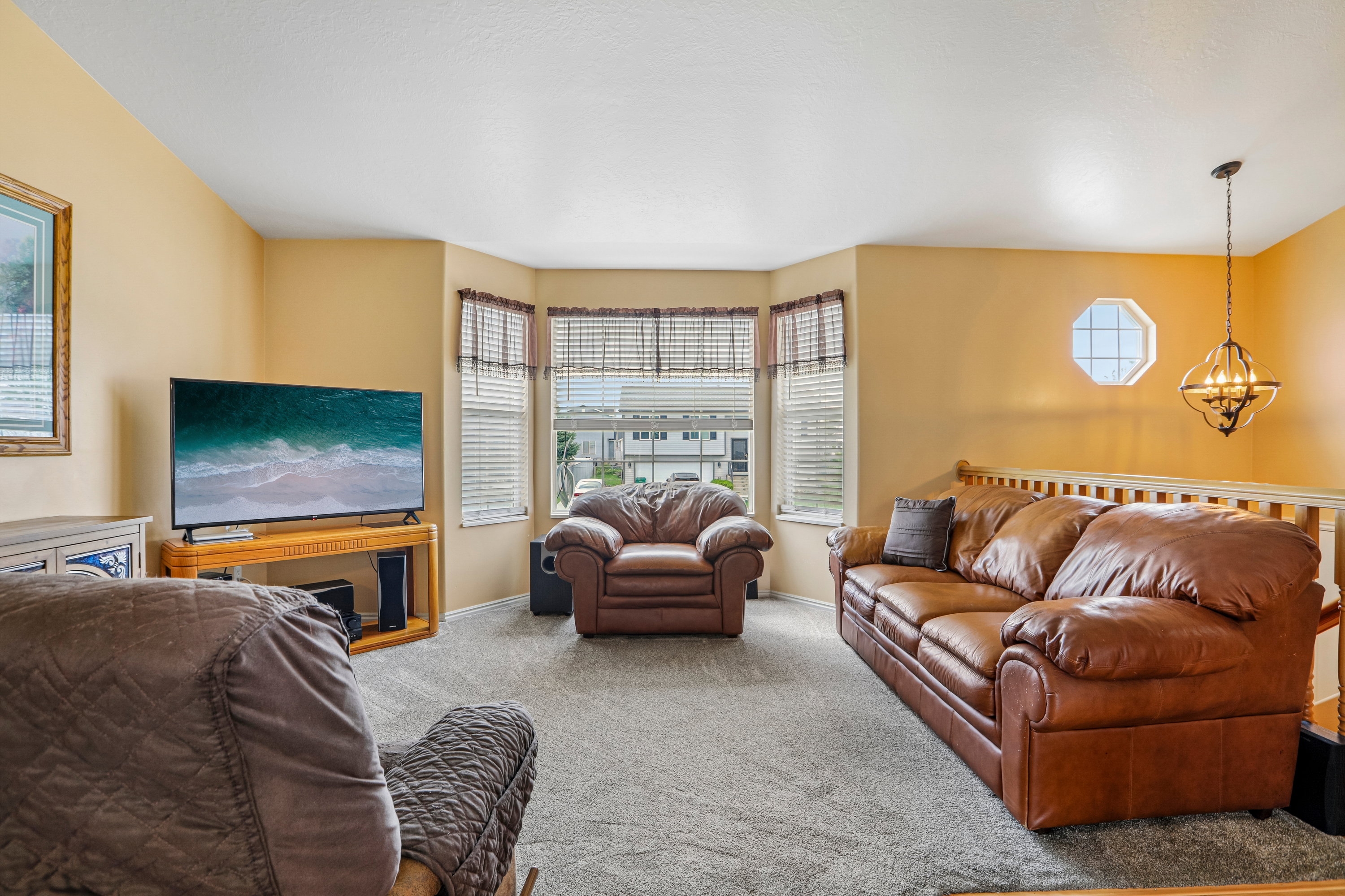 Living area featuring a bay window with blinds, carpeted flooring, a decorative octagonal window, and a chandelier-style light fixture