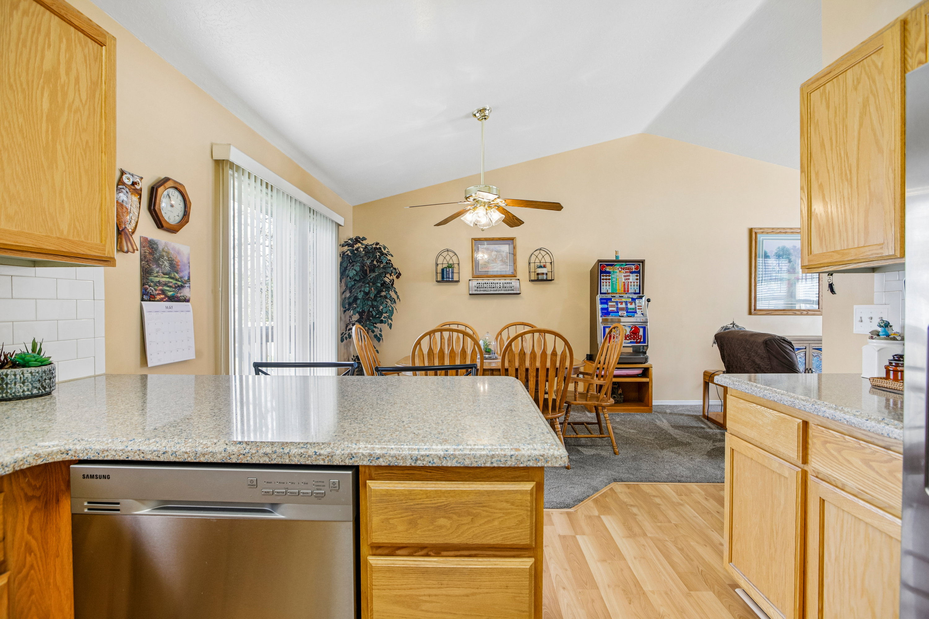Kitchen featuring wood-finish cabinetry, light-toned countertops, a stainless steel dishwasher, and a white subway tile backsplash