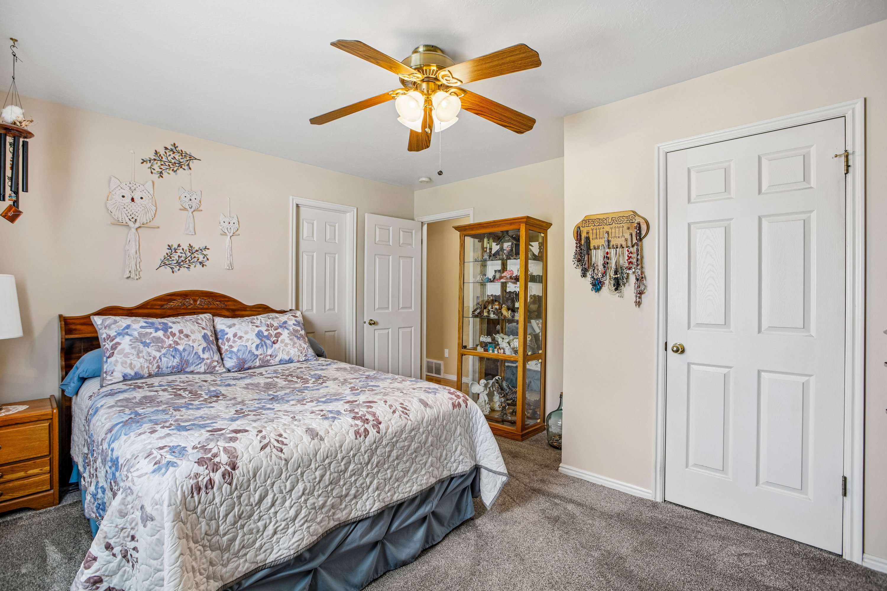 Bedroom featuring soft gray carpeting, light neutral walls, a multi-paneled door with a brass knob, and a ceiling fan with wood-finish blades