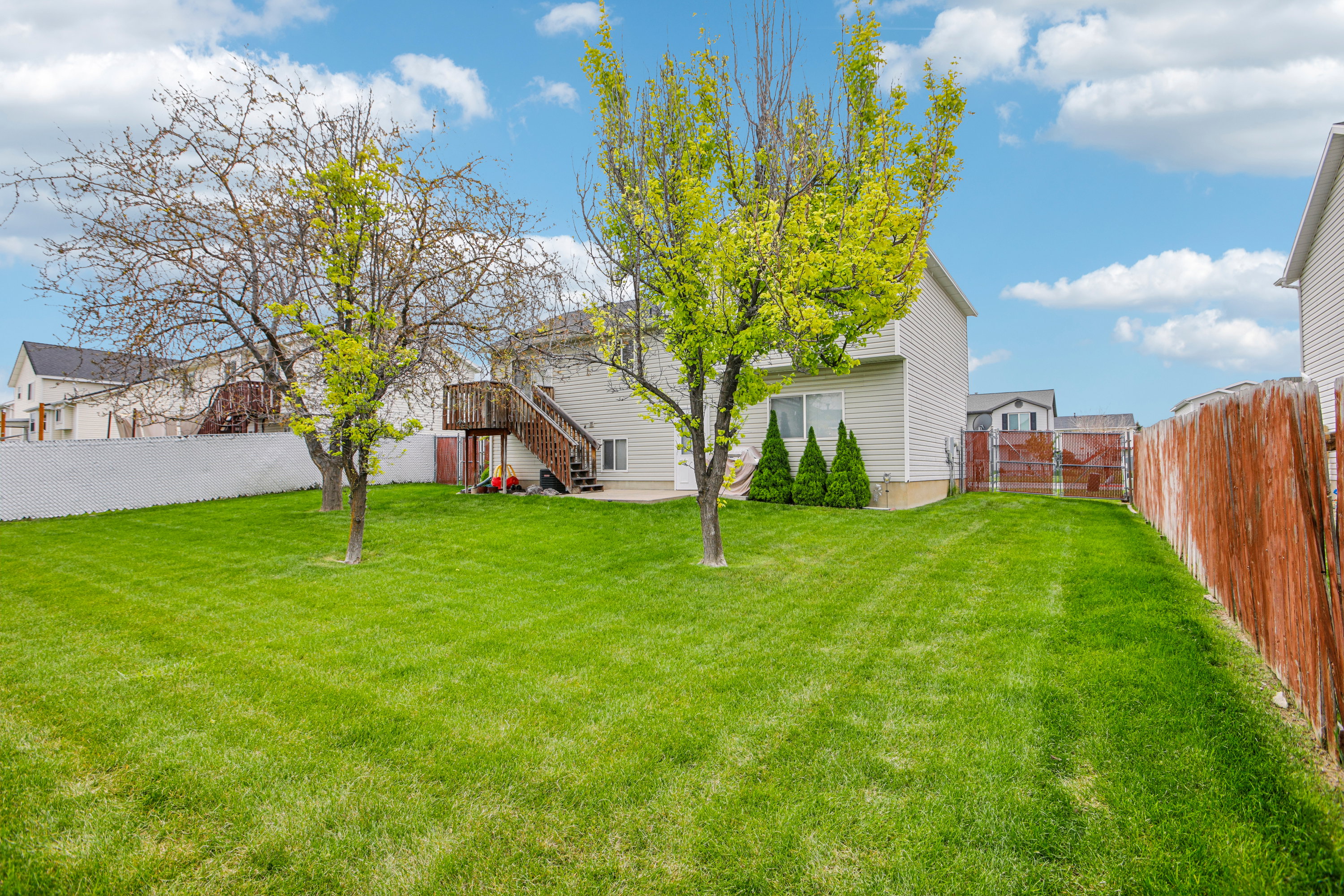 Expansive backyard featuring a large green lawn, mature trees, and a multi-level wooden deck with stairs