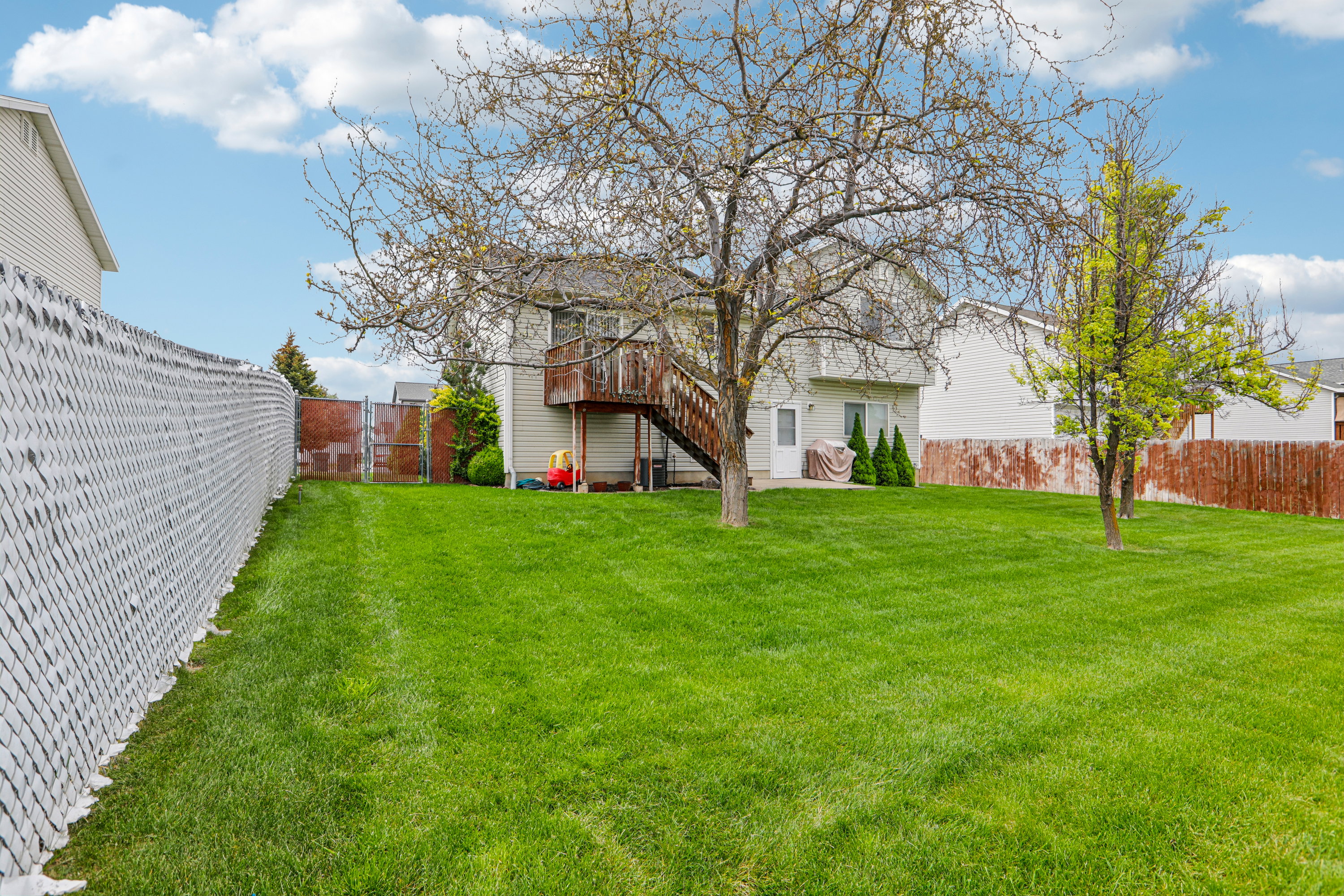 Spacious backyard featuring an expansive lawn, mature trees, a multi-level deck with stairs, a patio area, and a privacy fence
