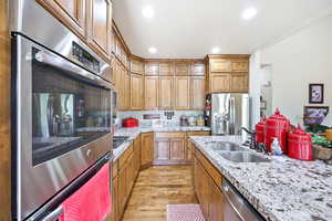 Kitchen featuring wood-finish cabinetry, granite-style countertops, stainless steel double oven, stainless steel refrigerator, and a double basin sink with a dark-finish faucet
