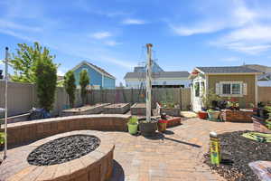 Expansive backyard featuring a paver patio with an integrated fire pit, raised garden beds, a detached storage shed with a white door and shutters, and mature landscaping