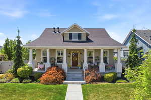 Craftsman-style home featuring a covered front porch with white columns, a dark shingle roof, and light tan siding