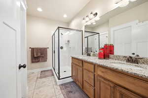 Bathroom featuring a dual vanity with light-colored countertops, wood-finish cabinetry, and a framed glass shower enclosure