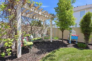 Backyard featuring a white pergola with climbing vines, a neatly mulched planting bed, and a well-maintained lawn