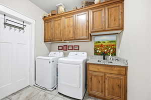 Laundry area featuring wood-finish cabinetry, a built-in sink with a stone-finish countertop, and tile flooring