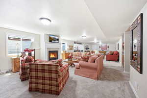 Spacious recreation room featuring light-colored carpeting, a fireplace with a white mantel, and multiple ceiling-mounted light fixtures