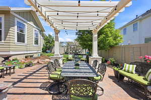 Brick paver patio with a white pergola, string lighting, and landscaping