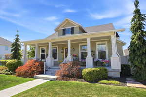 Craftsman-style home featuring a covered front porch with white columns, a dormer with black shutters, and mature landscaping