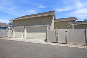 Exterior featuring two paneled garage doors, light-colored horizontal siding, dark shingle roofing, concrete driveway, and a light-colored privacy fence