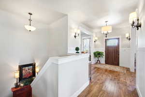 Entryway featuring wood-finish flooring, a solid wood front door with an integrated glass panel, and multiple wall sconces providing ambient lighting