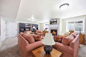 Living area featuring a fireplace with a white mantel, built-in black shelving, two windows, and wall-to-wall carpeting