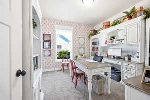 Dedicated office space featuring built-in white cabinetry and shelving, a light-colored wood-finish desktop, and grey carpeting