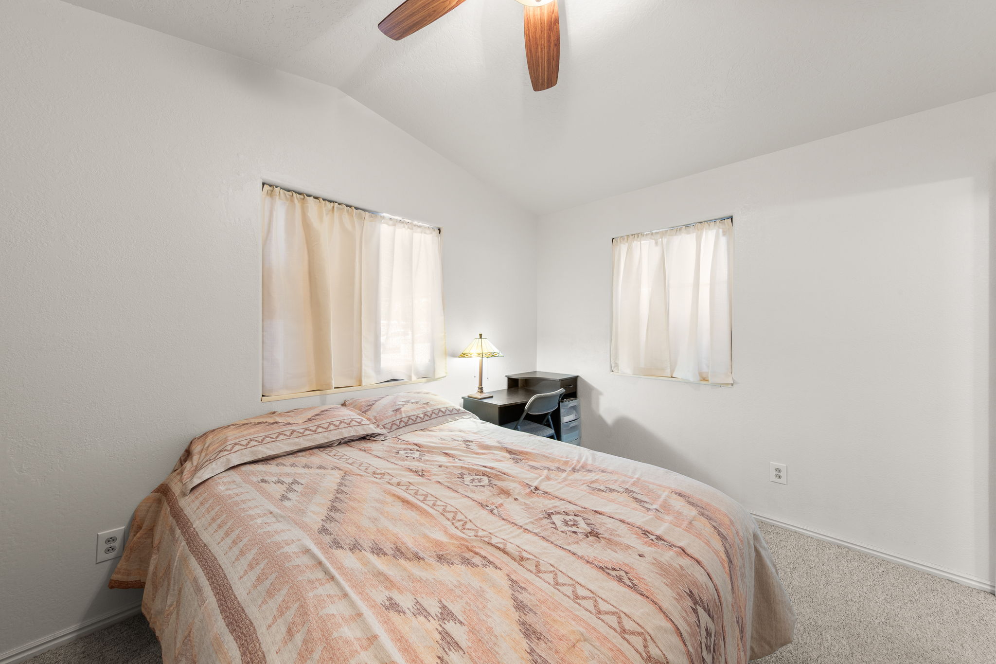 Room featuring vaulted ceilings, two windows, wall-to-wall carpeting, and a ceiling fan