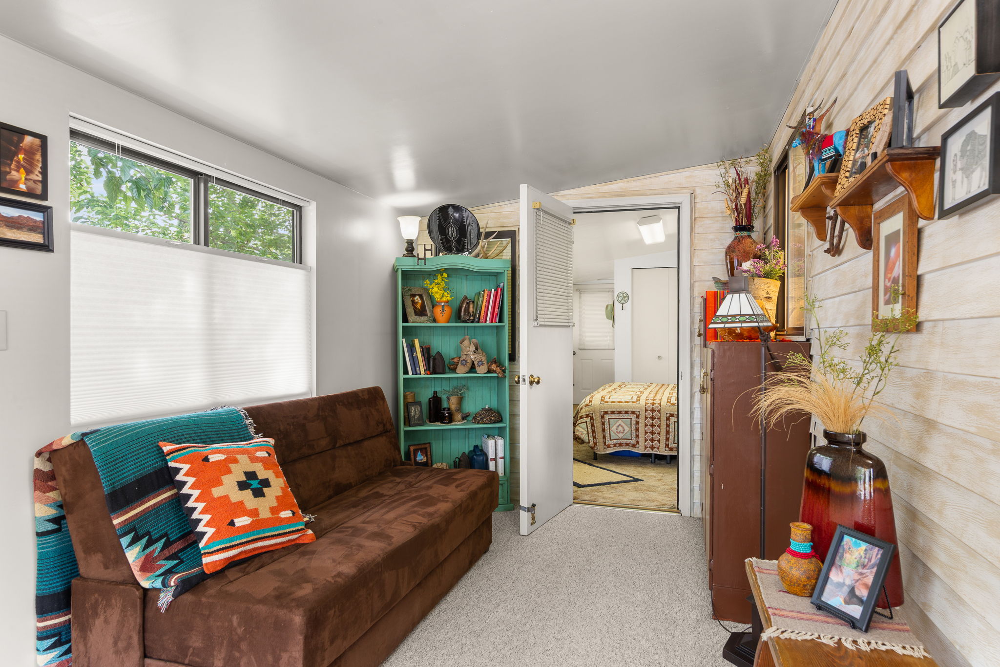 Carpeted interior space featuring a window with cellular shades, a shiplap accent wall, and a doorway opening to an additional room with carpet flooring