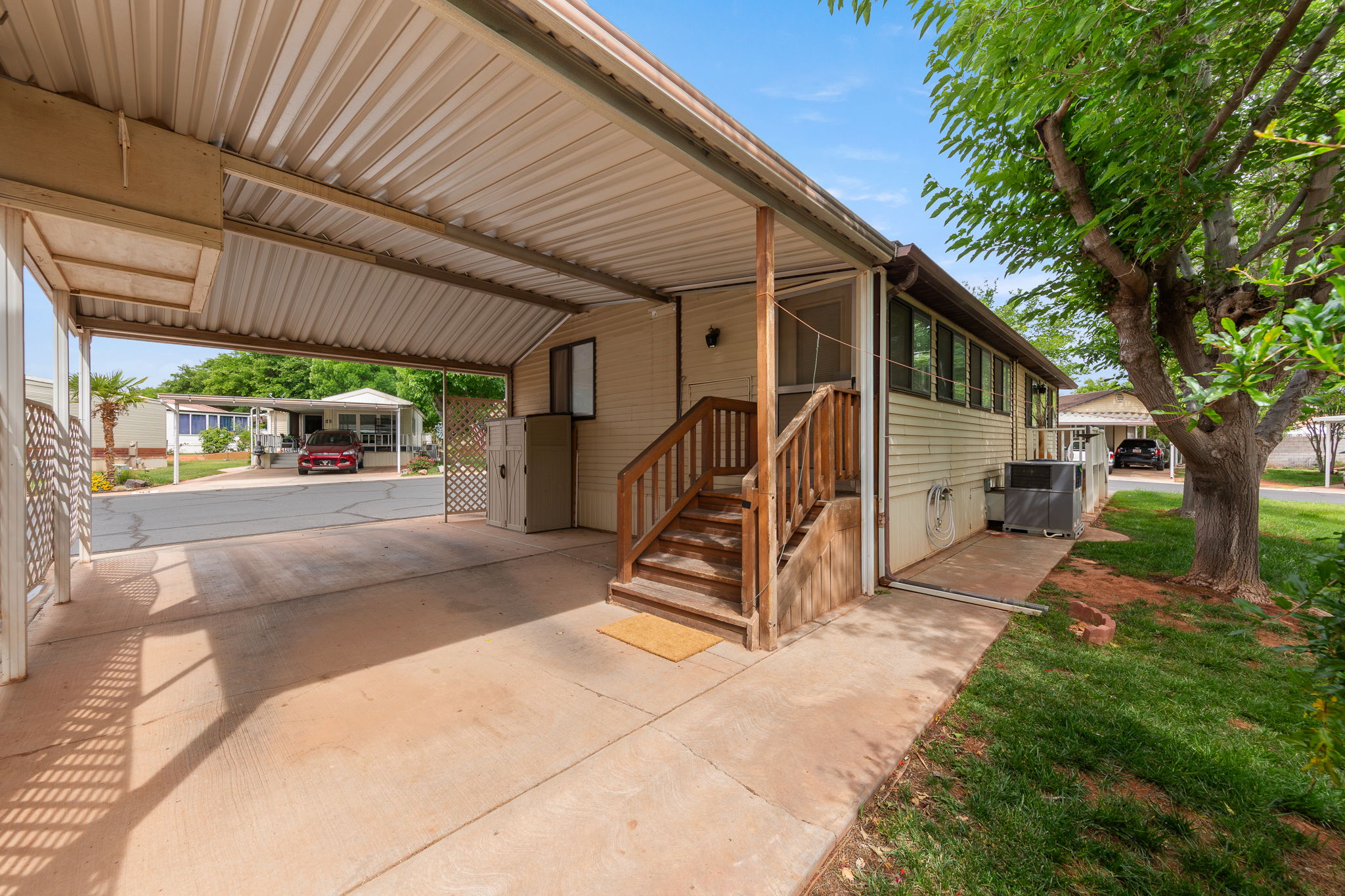 Concrete carport with a corrugated metal roof, a wooden staircase, and a lattice privacy screen
