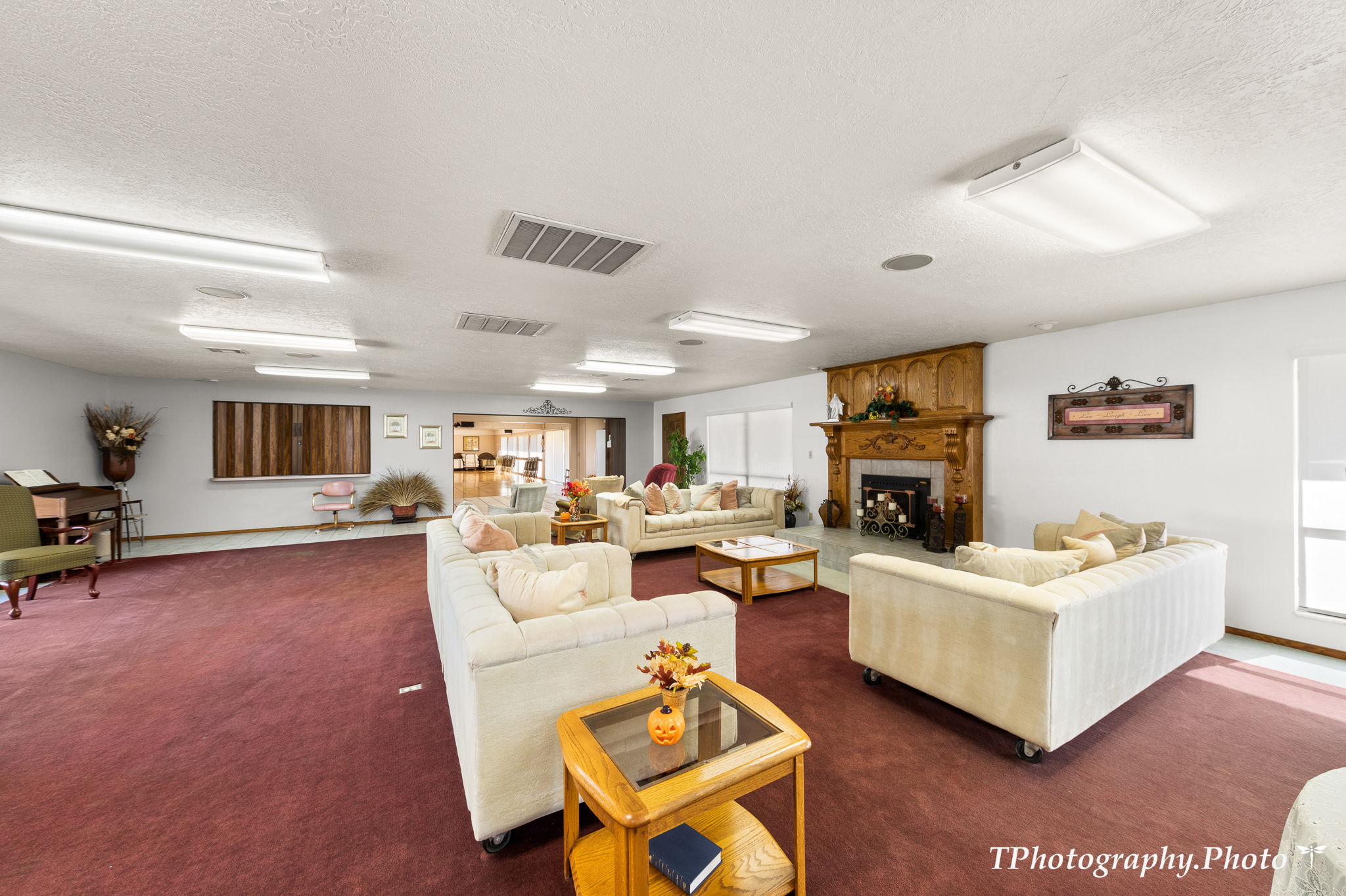 Spacious common area featuring a rich red carpet, multiple windows, and a prominent fireplace with an ornate wood mantel