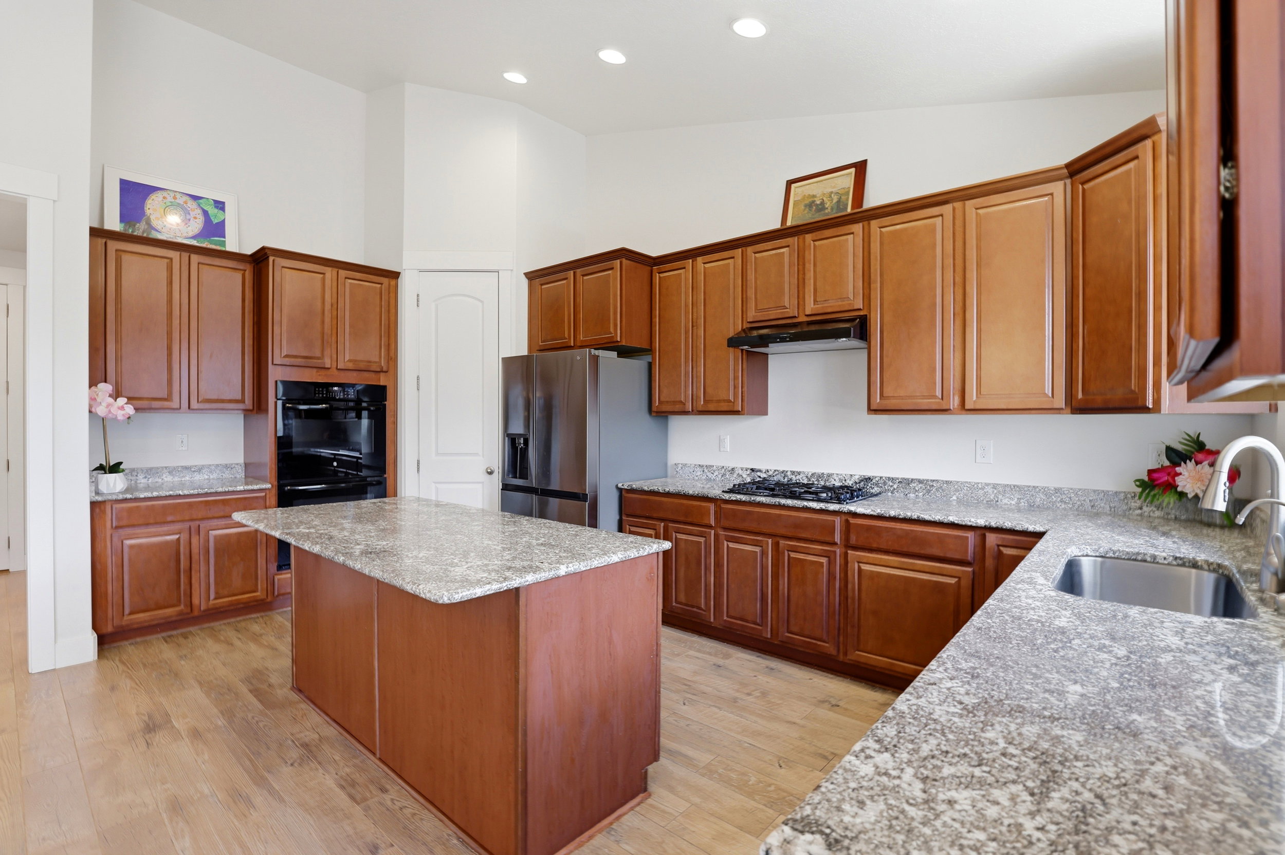 Well-appointed kitchen featuring light wood-finish flooring, a central island with granite countertop, abundant wood cabinetry, stainless steel appliances, and recessed lighting