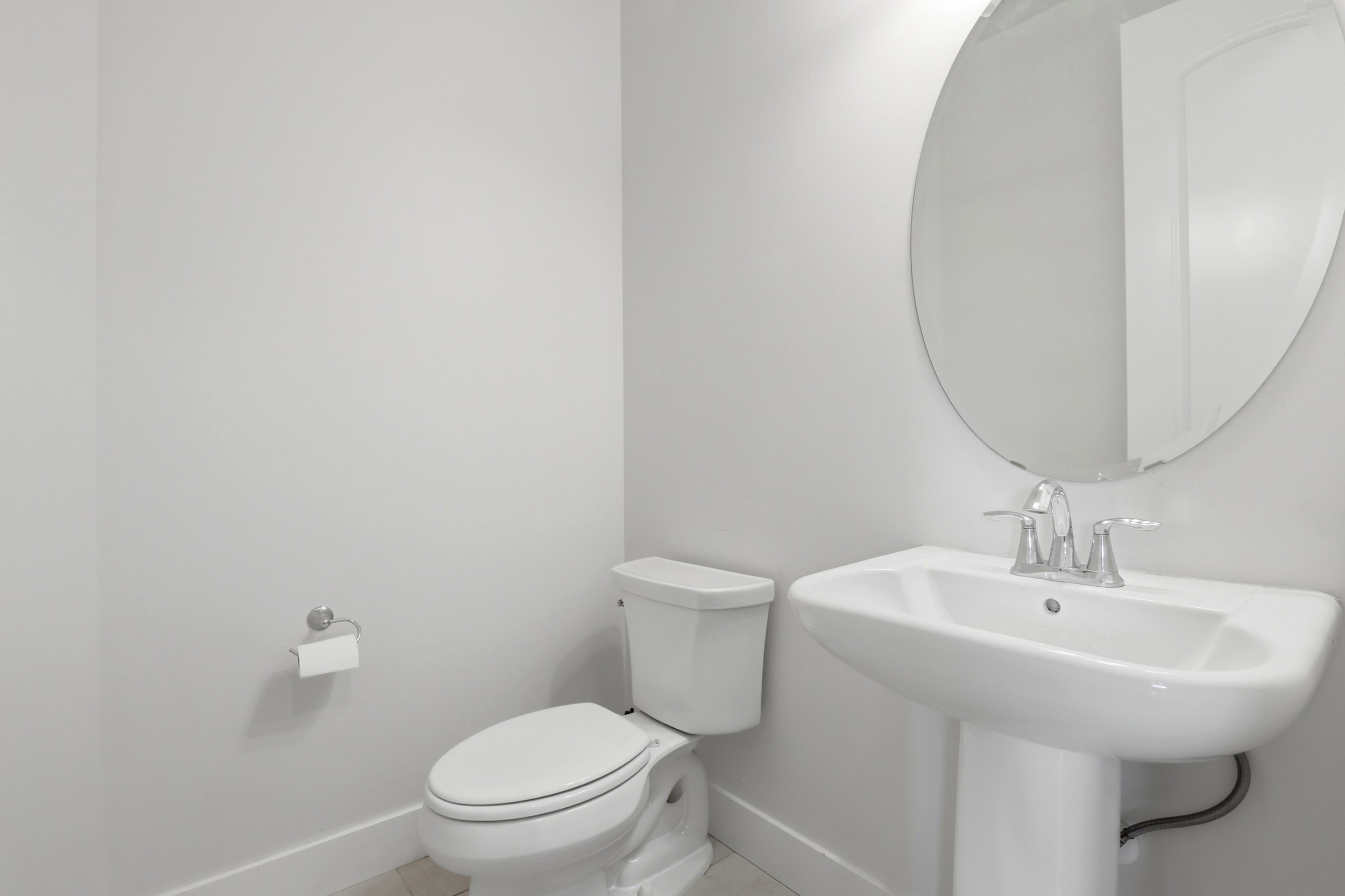 Pedestal sink with chrome faucet, oval mirror, and white toilet