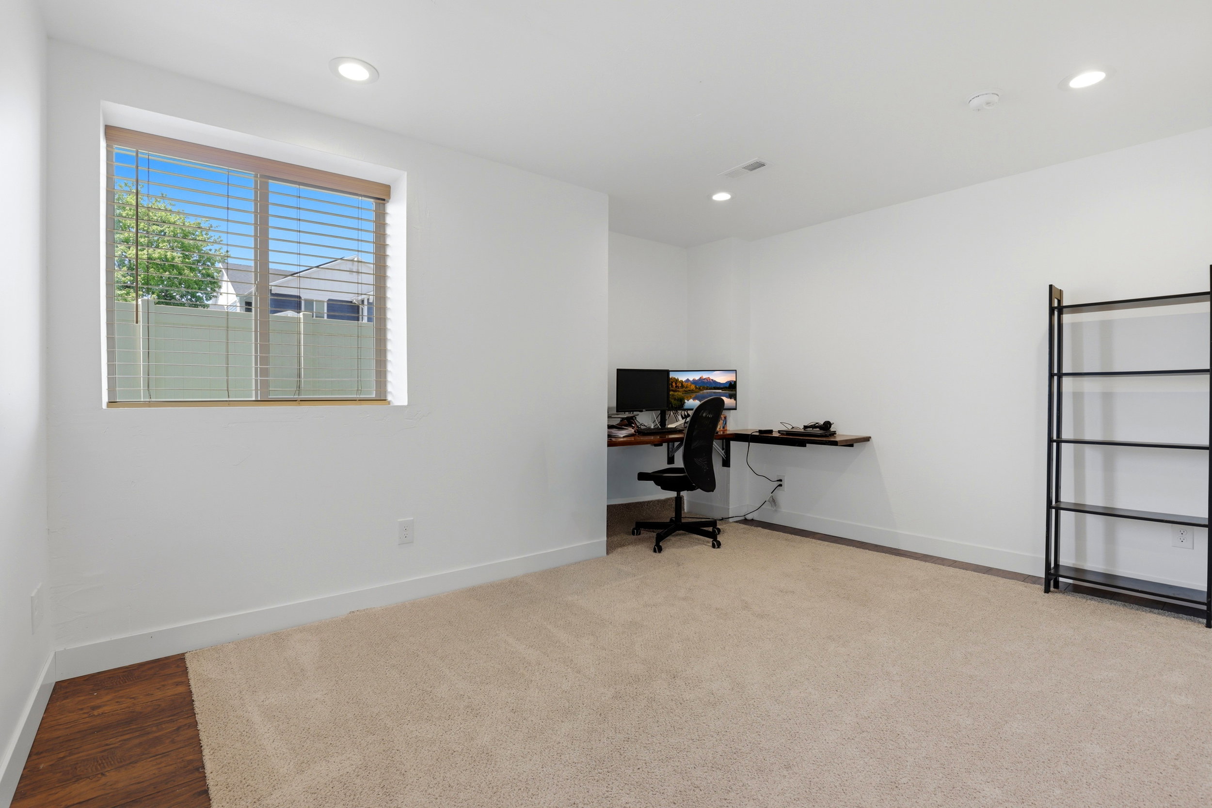 Bright room featuring recessed lighting, a window with horizontal blinds, neutral-toned carpet, white baseboards, and a dedicated corner with wood-finish flooring