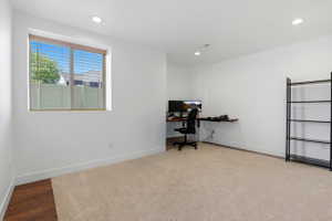 Bright room featuring recessed lighting, a window with horizontal blinds, neutral-toned carpet, white baseboards, and a dedicated corner with wood-finish flooring
