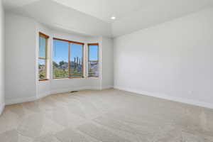 Spacious room featuring a bay window with natural wood trim and horizontal blinds, recessed ceiling lighting, and light-toned carpeting