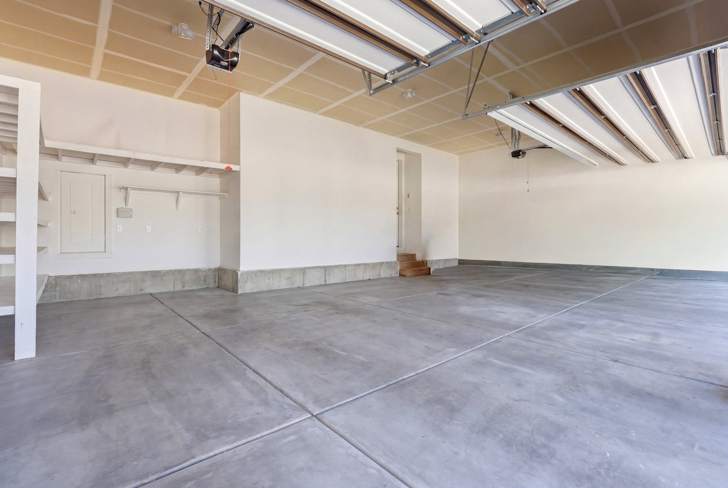 Spacious garage featuring a concrete floor, built-in shelving, overhead lighting, and an automatic garage door opener