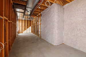 Unfinished basement framing with exposed lumber studs, concrete flooring, insulated perimeter walls, visible ductwork, and electrical conduit