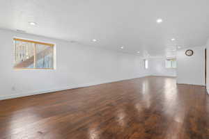 Expansive room featuring rich wood-finish flooring, recessed lighting, multiple windows with blinds, and white painted walls