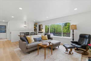 Open-concept living area featuring light wood-finish flooring, recessed lighting, a large picture window, and built-in shelving
