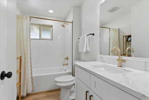 Bathroom featuring a white subway tile shower surround, a full vanity with a white countertop and integrated sink, gold-tone fixtures, and wood-finish flooring