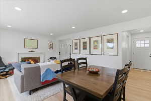 Open-concept living area featuring a fireplace with a white mantel, light wood-finish flooring, recessed lighting, and a front entry door with multiple glass panes