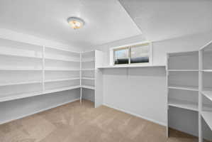 Room featuring extensive built-in white shelving, recessed window, and light-toned carpet flooring