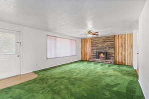 Living space featuring a stone fireplace with a metal grate, wood-paneled walls, and a ceiling fan