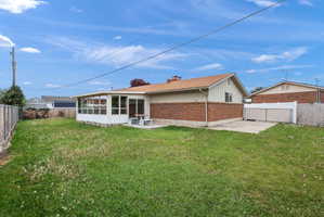 Rear exterior featuring a sunroom addition, concrete patio, and a chain-link fence